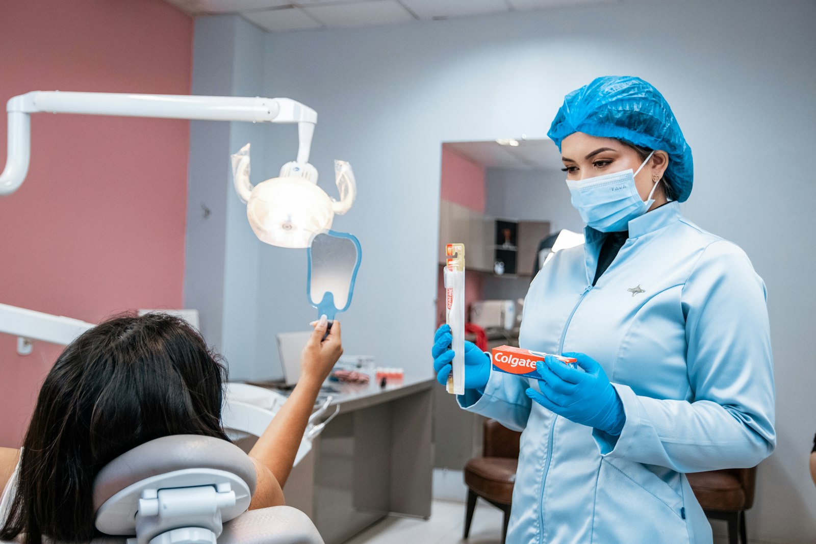 Dentist showing a child in the dental chair how to brush, while the child holds a hand mirror